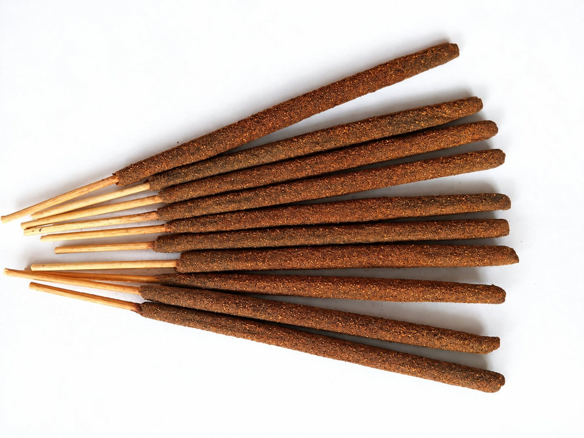 Brown handmade incense sticks fanned out on a white background.