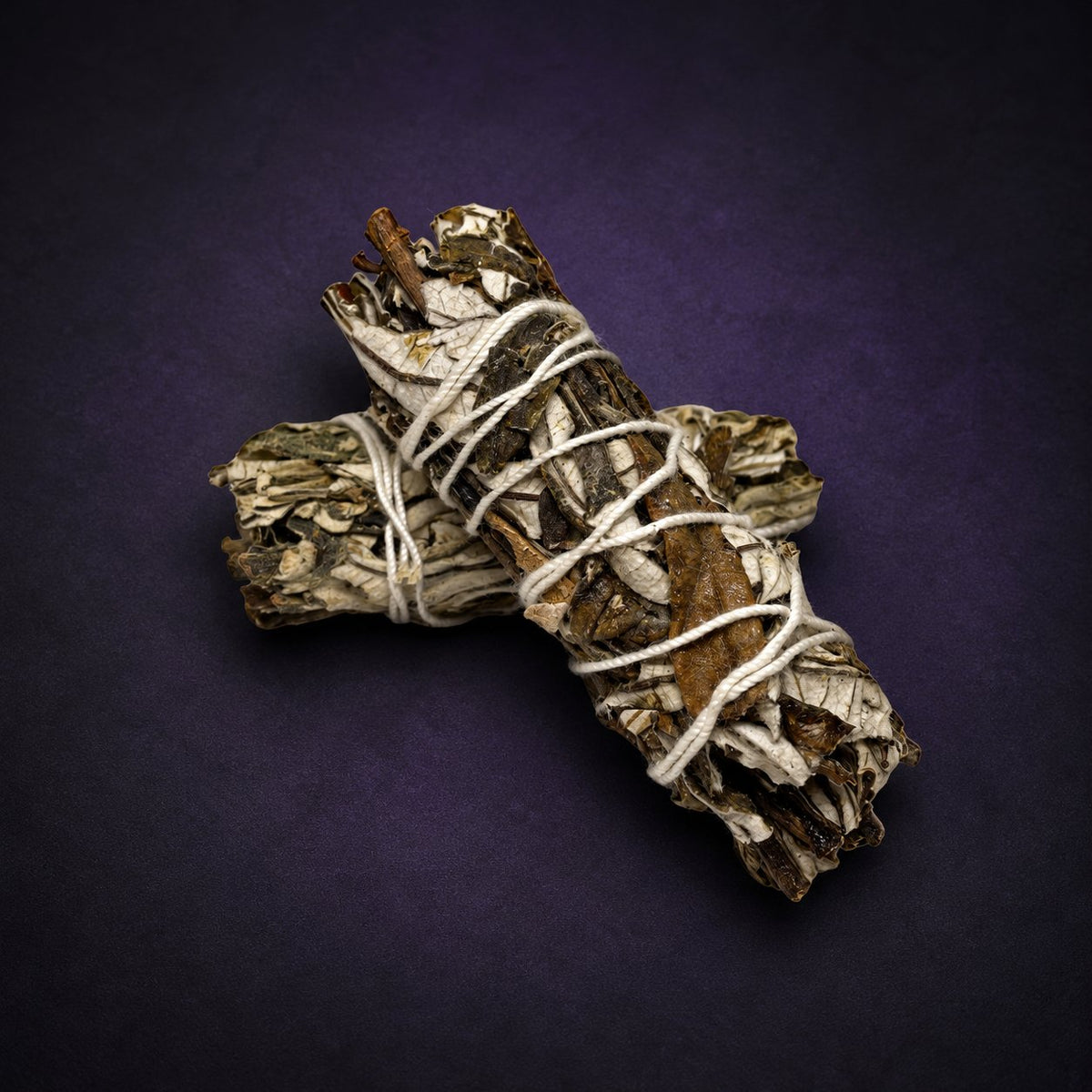 Two dried Yerba Santa bundles crossed and tied with cotton twine on a charcoal and subtle purple background.