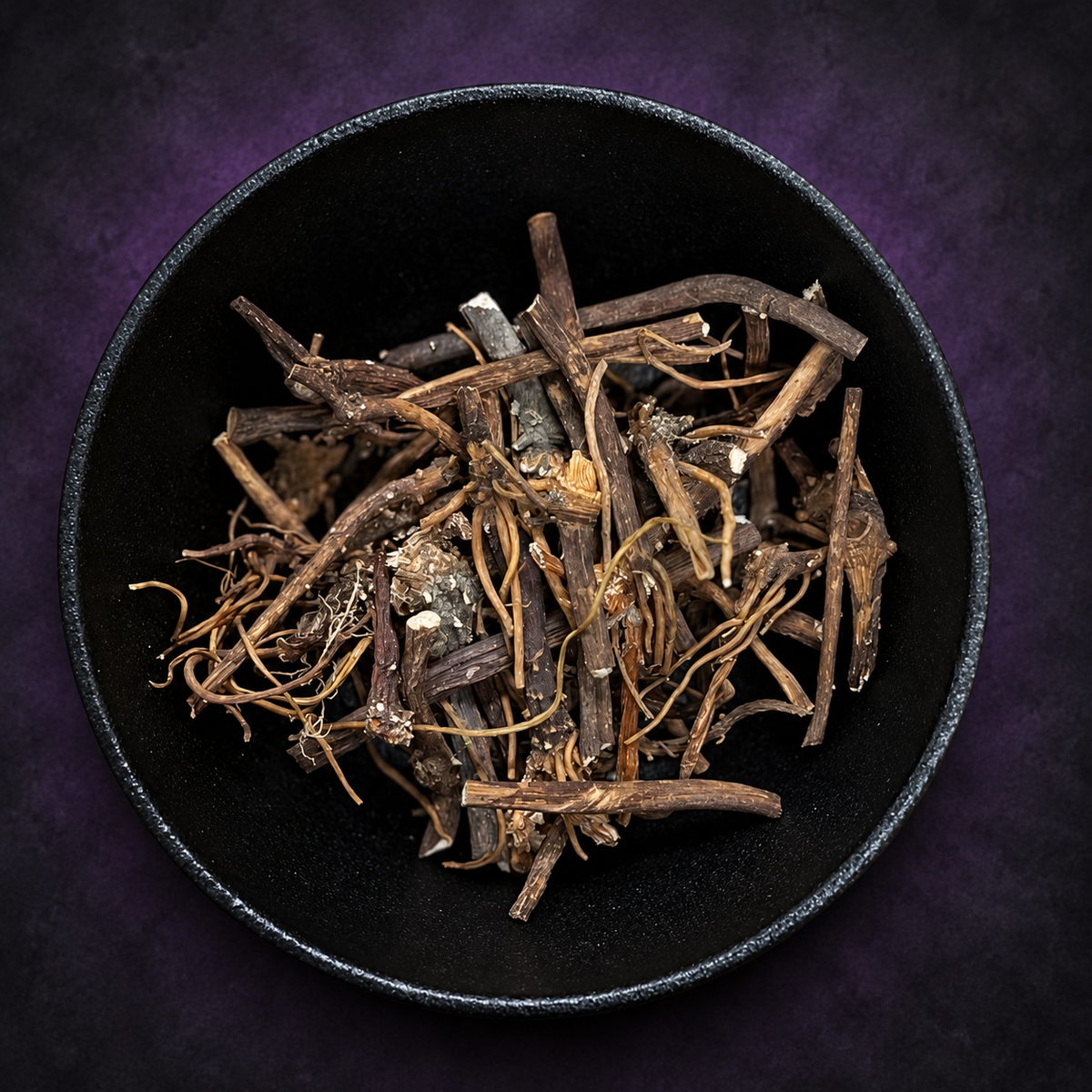 Dried mandrake root pieces in a black bowl on matte charcoal and deep royal-purple background.
