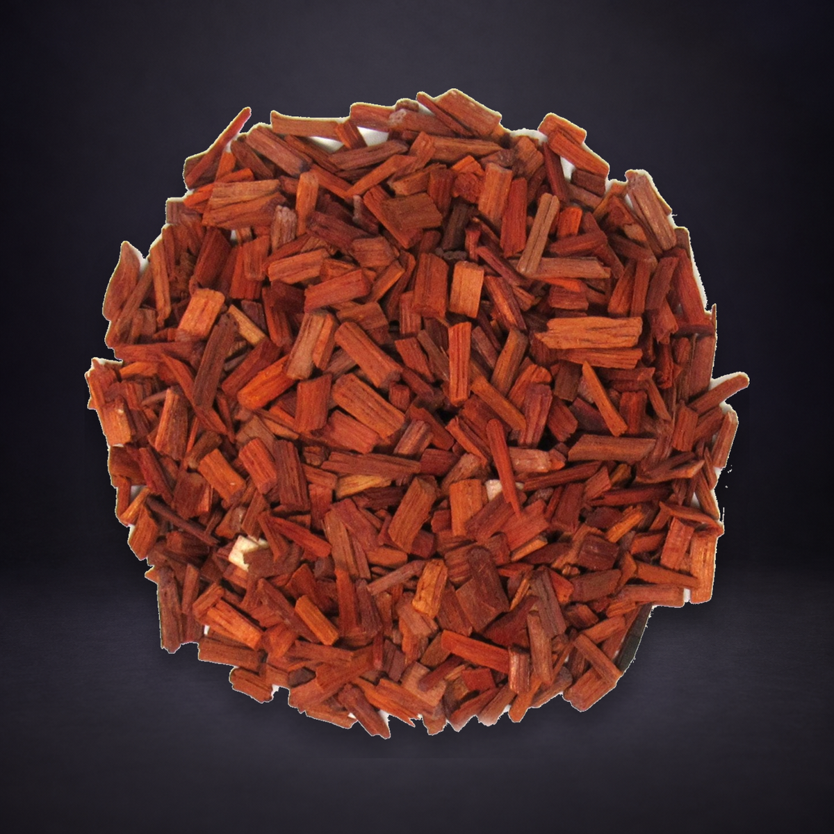Red sandalwood chips in the original black dish on a matte charcoal and subtle royal-purple background.